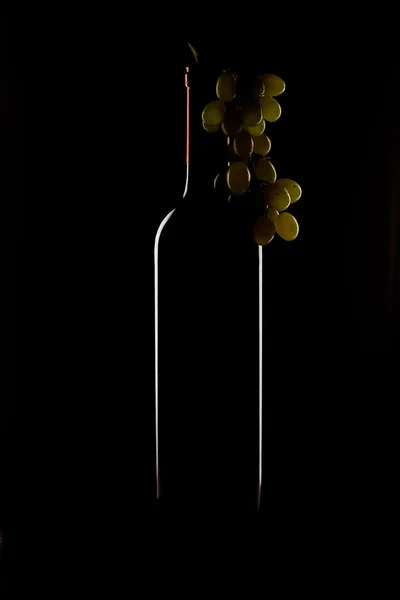 Botella de vino y un racimo de uvas sobre un fondo negro — Foto de Stock