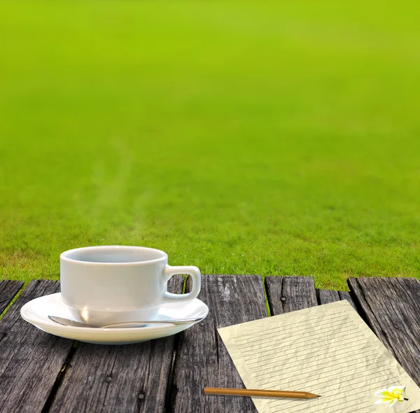 Caffè caldo e carta da lettera sul tavolo in legno con giardino in erba — Foto Stock
