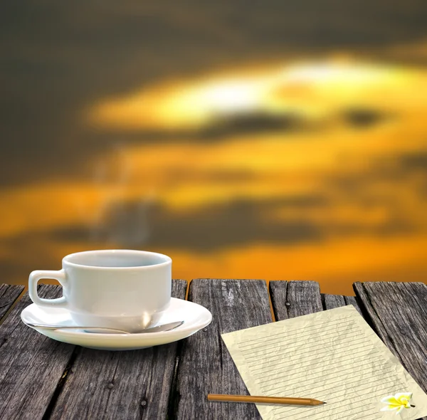 Чашка кави і літера на дерев'яному столі з небом заходу сонця — стокове фото