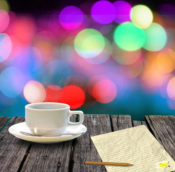 Sıcak kahve ve letter kağıt üzerinde renkli bokeh arka plan ile ahşap masa — Stok fotoğraf