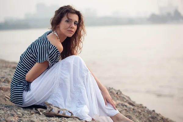 Brunette vrouw zittend op stenen strand — Stockfoto