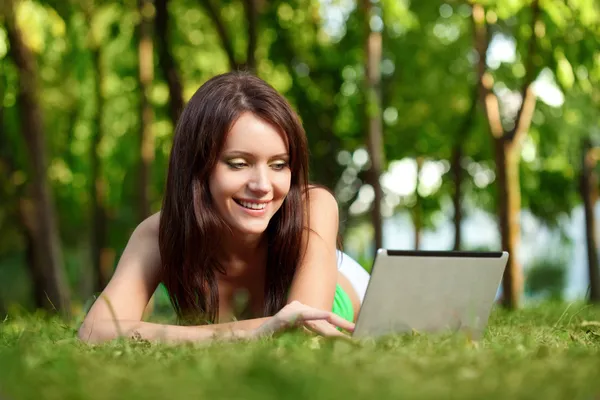 Щаслива жінка лежить на траві з ноутбуком — стокове фото
