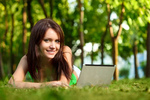 Frau liegt mit Laptop im Gras Stockbild