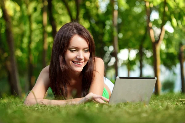 Glückliche Frau liegt mit Laptop im Gras Stockfoto