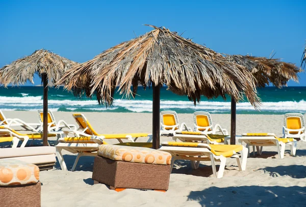 Sonnenschirme mit Liegestühlen am Strand unter blauem Himmel — Stockfoto