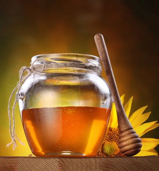 Miel en un frasco de vidrio y girasol flor —  Fotos de Stock