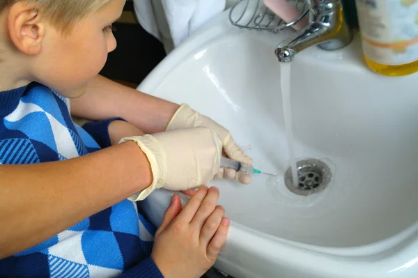 The boy looks at the doctor's hands in gloves, holding a syringe — Stock Photo, Image
