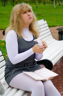 The schoolgirl sitting on a bench and tore pages of the diary clipart