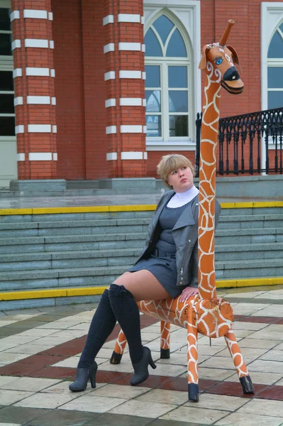 La fille est assise sur un banc sous la forme d'une girafe — Photo