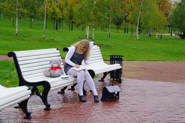 Den skolflickas satt på en bänk i höst park — Stockfoto