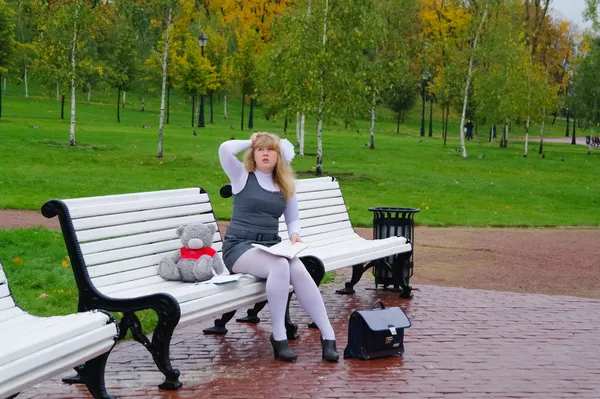 De schoolmeisje zittend op een bankje in de herfst park — Stockfoto