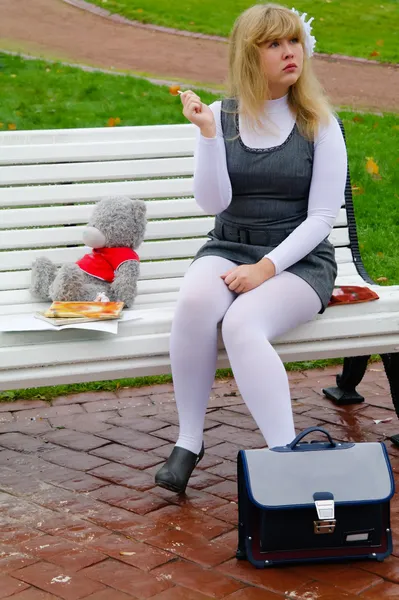 Школярка сидить на лавці з білими цукерками — стокове фото