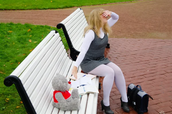 Den skolflickas satt på en bänk i höst park — Stockfoto