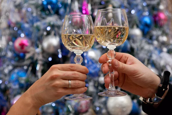 Manos sosteniendo copas de champán contra el árbol de año nuevo —  Fotos de Stock