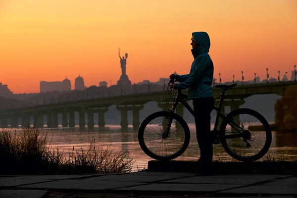 Jeune femme avec vélo contre le ciel au coucher du soleil — Photo