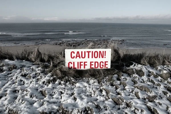 Red caution sign on cliffs slippery edge — Stock Photo, Image