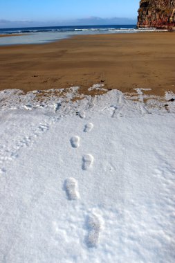 Footprint tracks in snow on empty beach on a cold winters day clipart