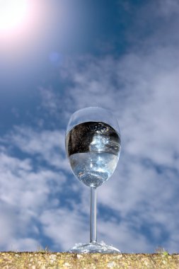 Glass of water against a glaring sunny sky clipart