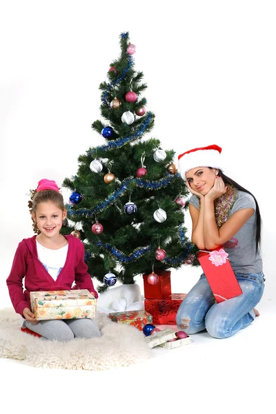 Mother and daughter near a christmas tree with gifts, isolated on a white b — Stock Photo, Image