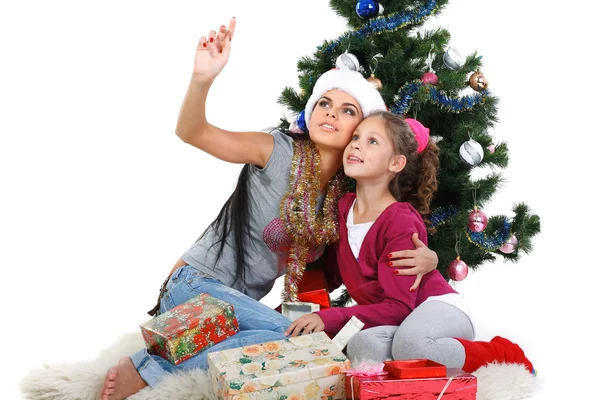 Mother and daughter near a christmas tree with gifts, isolated on a white b — Stock Photo, Image