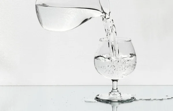 Sklenice na víno na zrcadle je naplněn vodou ze džbánu — Stock fotografie