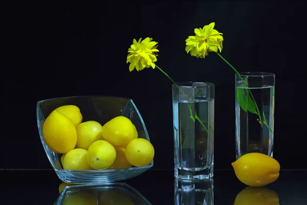 Två glas med blommor och en glasskål med gula tomater — Stockfoto
