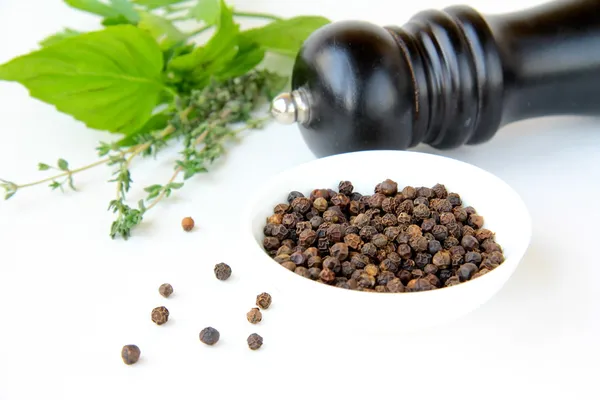 Black pepper in a bowl and herbs — Stock Photo, Image