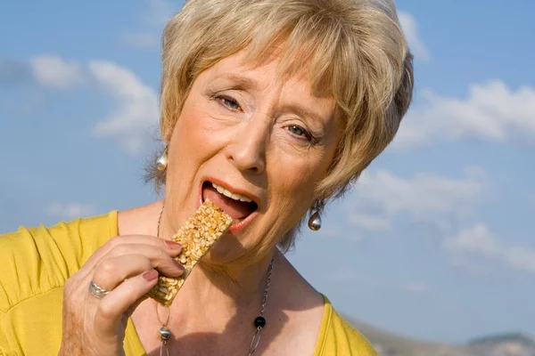 Feliz mujer mayor comiendo barra de cereal saludable — Foto de Stock