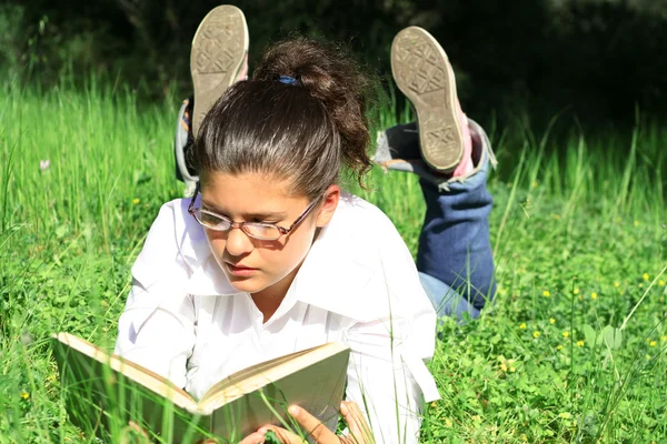 Девочка на траве читает книгу на открытом воздухе летом в кампусе — стоковое фото