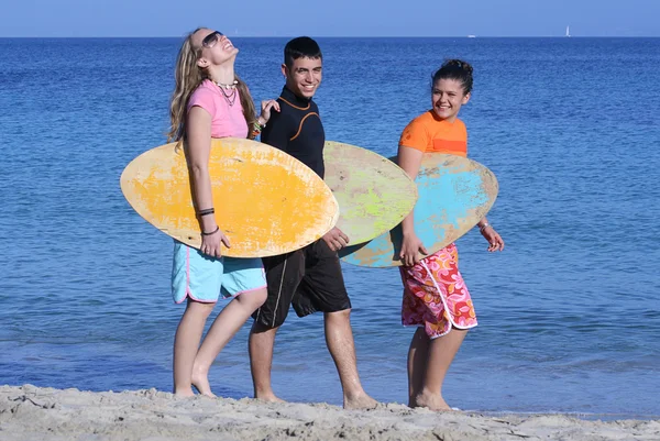 Jóvenes surfistas caminando por la playa felices y sonrientes —  Fotos de Stock