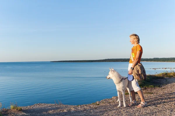 Kobieta z kosztami psa na skraju pęknięcia na morzu — Zdjęcie stockowe