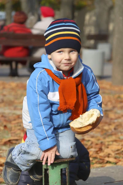 Ребенок ест хлеб во время осенней прогулки в парке — стоковое фото