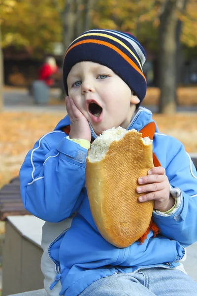 The kid eats bread during autumn walk in the park — Stockfoto