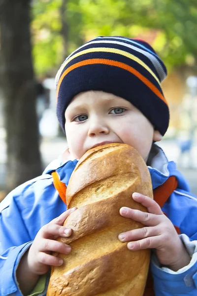 The kid eats bread during autumn walk in the park — Stockfoto