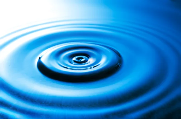 Droplet faller i blått vatten — Stockfoto