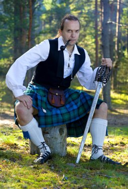 Man in scottish costume with sword and pipe clipart