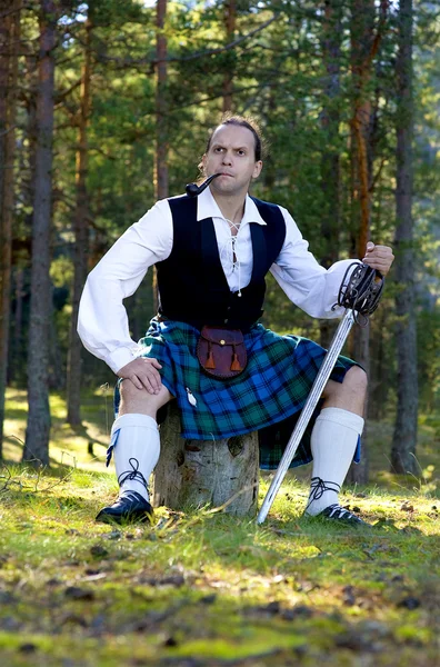 Человек в шотландском костюме с мечом и трубкой — стоковое фото