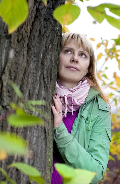 Blond kvinna som tittar från trädet — Stockfoto