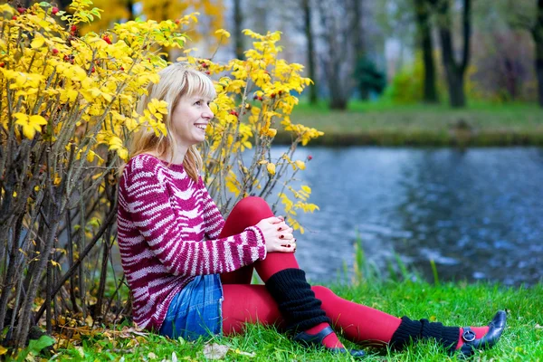 Blonďatá žena sedí na břehu řeky — Stock fotografie