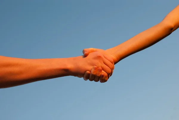 Ruce třást navzájem proti modré obloze — Stock fotografie