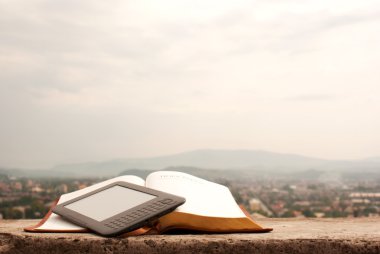 Electronic book reader laying on the book outdoors clipart