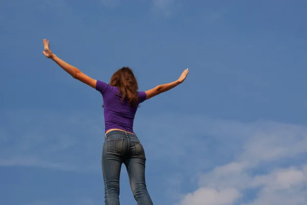Молодая женщина, стоящая с поднятыми руками на голубом небе — стоковое фото