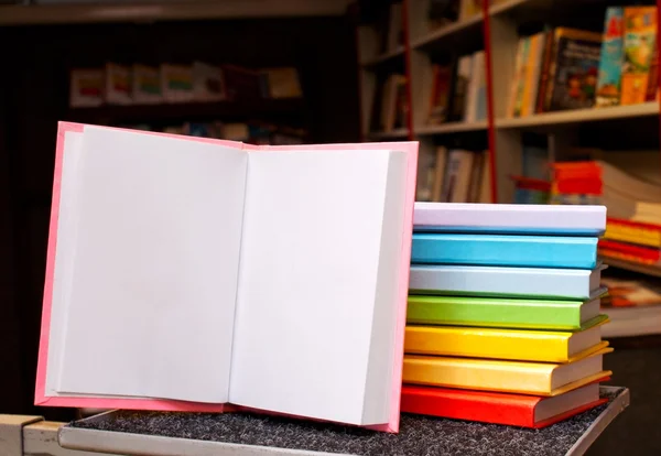 Offenes Buch mit einem Stapel bunter Bücher dahinter — Stockfoto