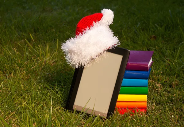 Leitor de livros eletrônicos usando chapéu de Papai Noel com pilha de livros — Fotografia de Stock