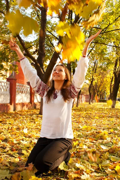 stock image Young lady playing with leaves in a park at fall time