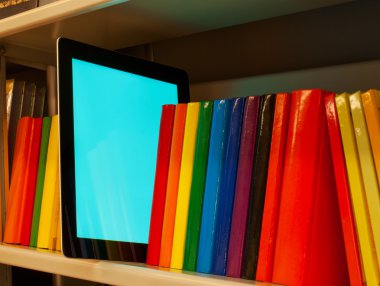 Row of colorful books and electronic book reader on the shelf clipart