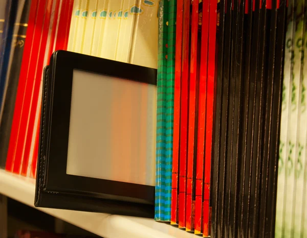Fila di libri colorati e lettore di libri elettronici sullo scaffale — Foto Stock