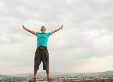 Young man staying with raised hands against blue sky clipart