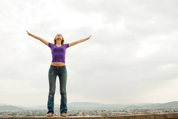 Jovem mulher ficar com as mãos levantadas contra o céu azul — Fotografia de Stock