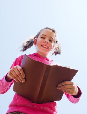 Teen girl reading the Bible against blue sky clipart